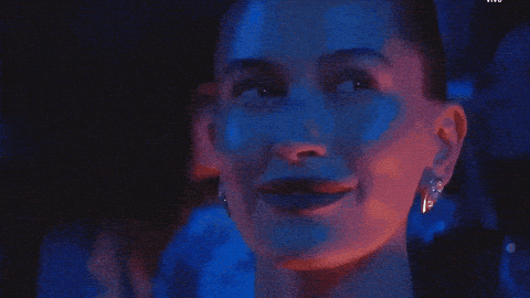 GIF de Hailey Bieber affichant un sourire confiant et satisfait sous des lumières colorées pour illustrer la réussite et la sérénité après le déploiement d'un plan de communication efficace.